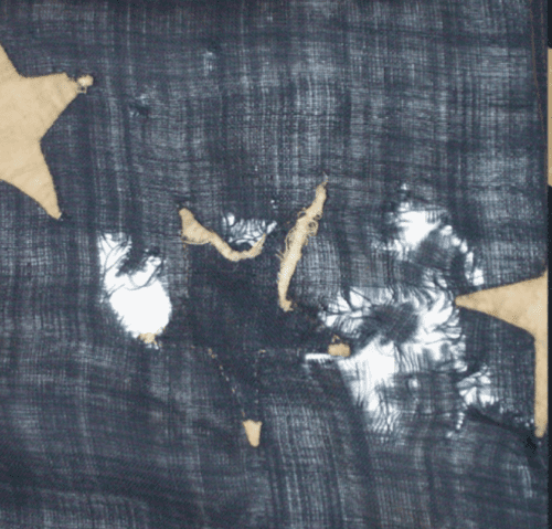 Pale star appliqués on a dark textile ground, showing areas of fabric loss and fraying between the stars.